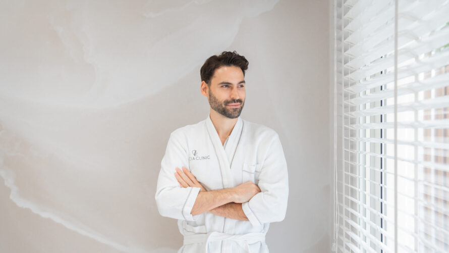 A man in a robe next to a window, thinking about why more men are choosing preventative aesthetics in their 30s and 40s